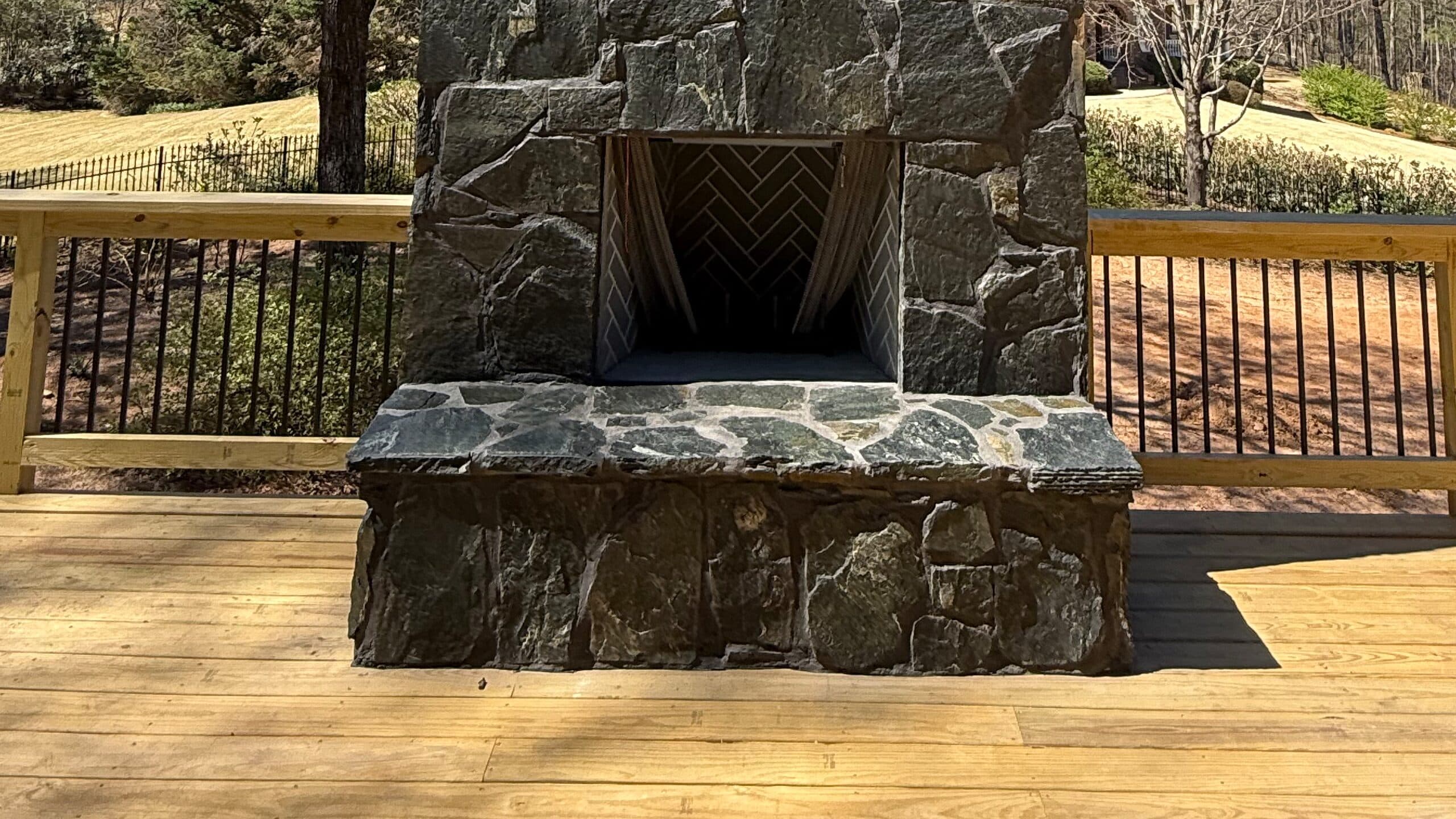 Chimenea exterior de piedra terminada, con fogón en espiga sobre una terraza de madera