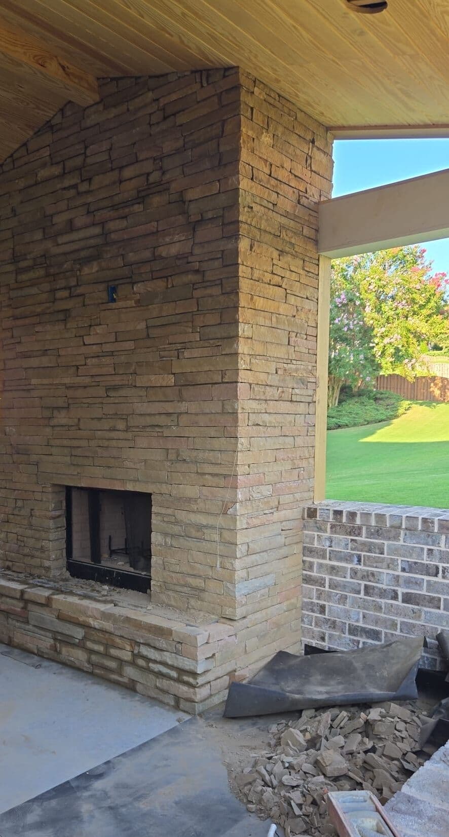 Stacked stone fireplace nearly complete under the pine porch ceiling