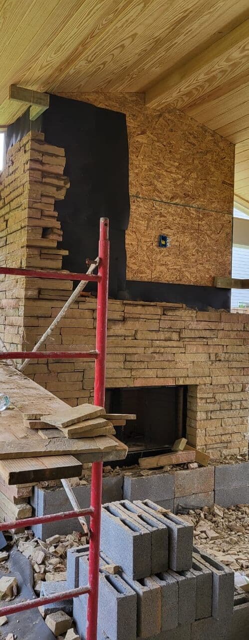 Fireplace chase wrapped in board and black membrane, stone veneer rising from the firebox