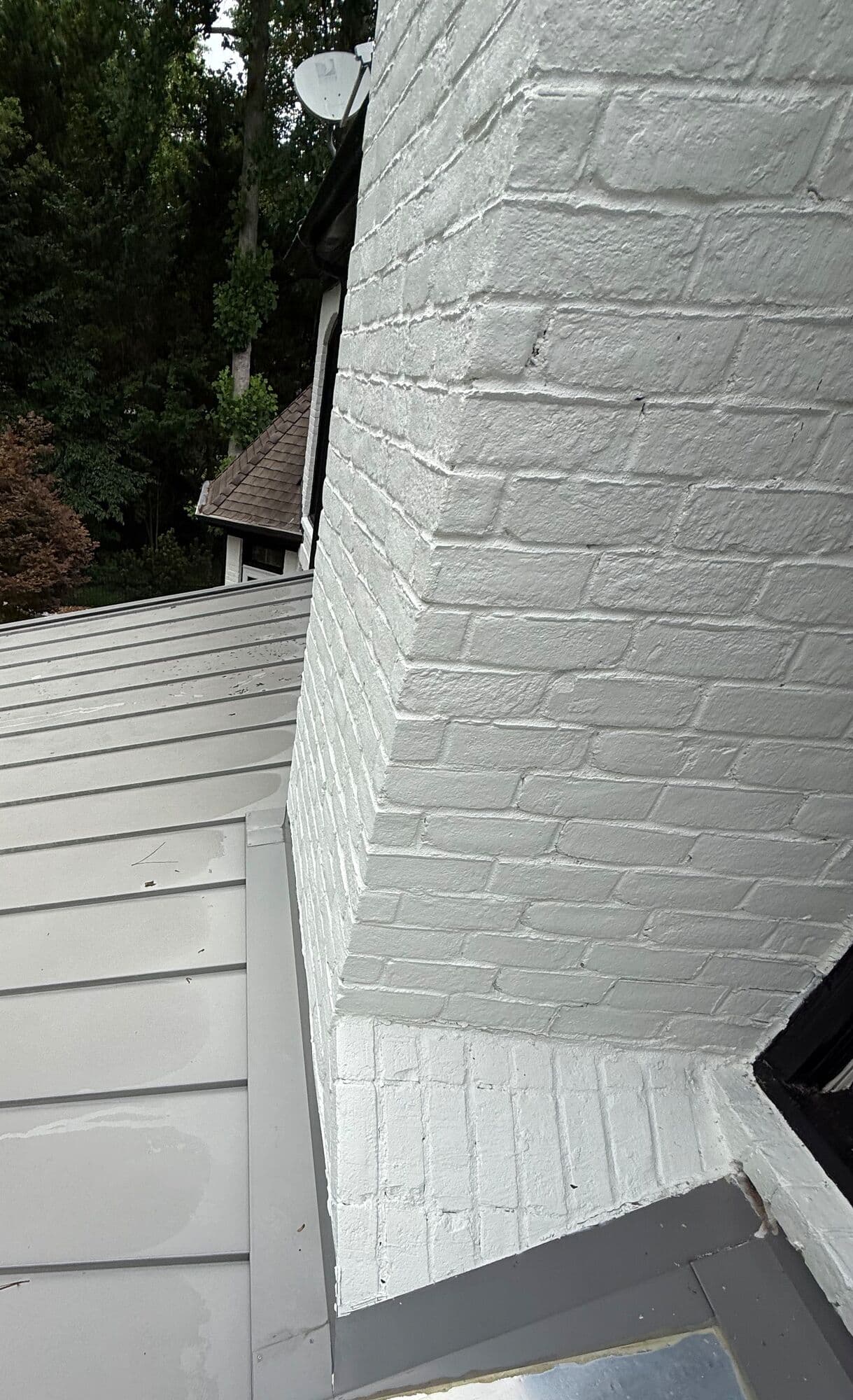 Chimney base and roof flashing seen from above along the metal roof