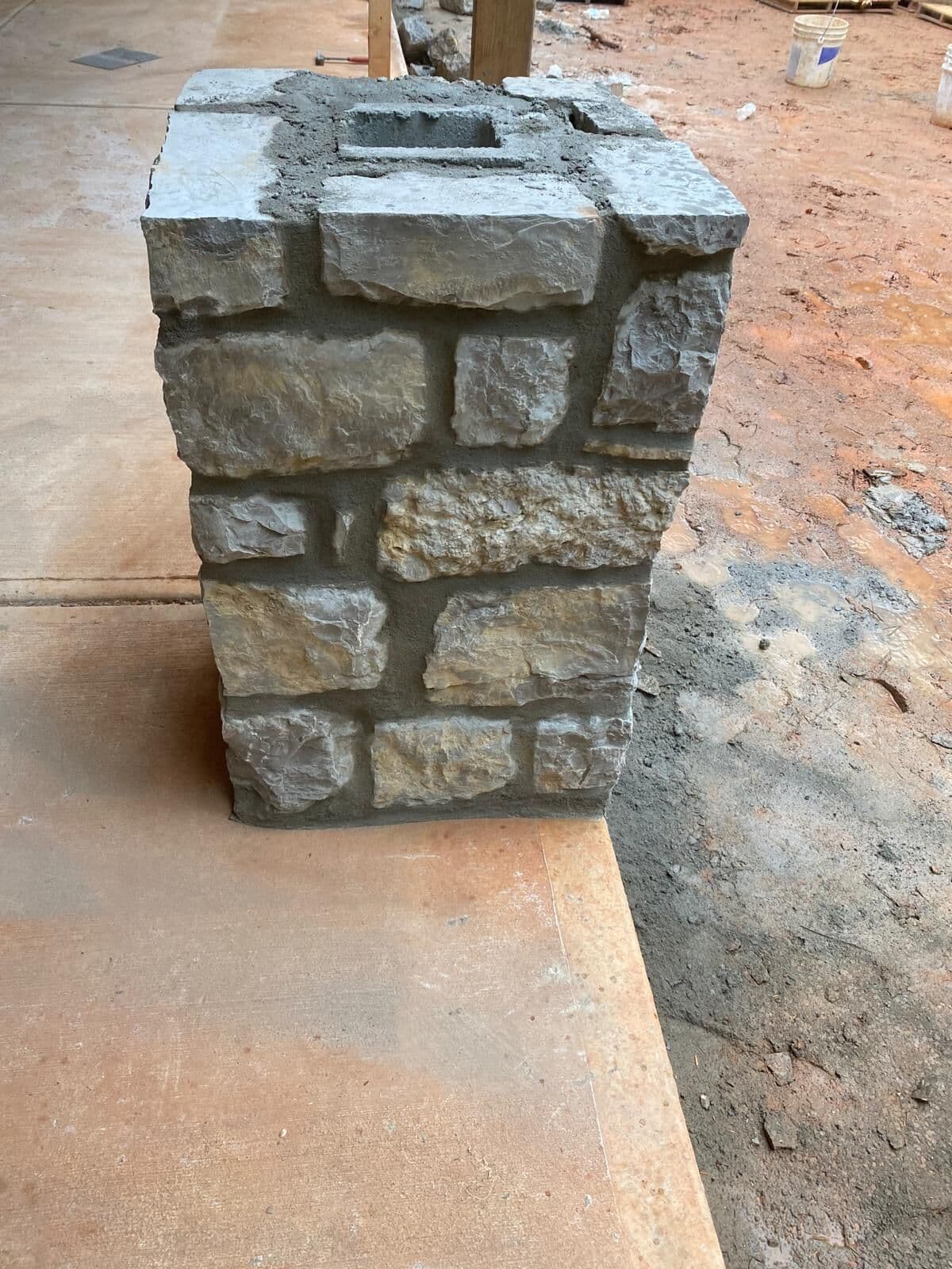 Finished natural stone column base with a mortared cap, seen from the corner on a concrete slab