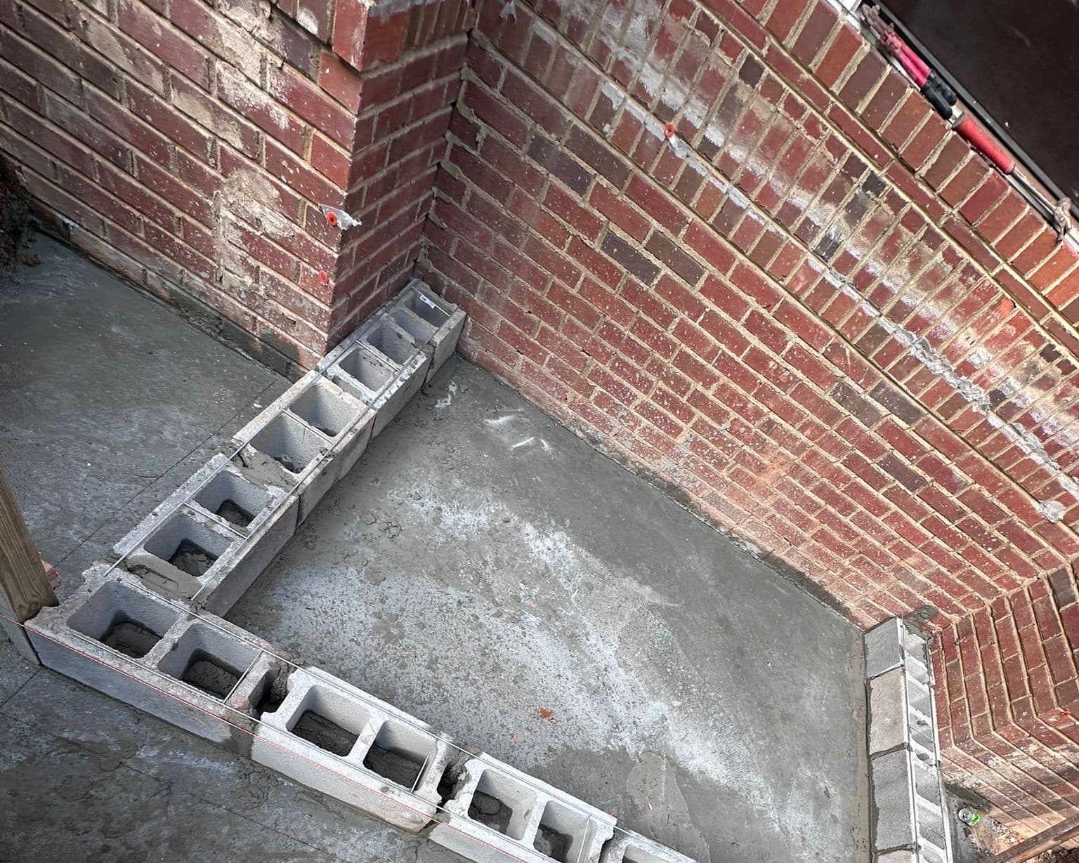 First course of concrete block set in an L on the slab against the brick wall