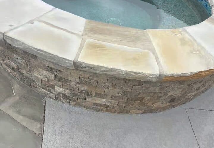 Muro del spa en piedra apilada con remate de piedra, junto a la piscina